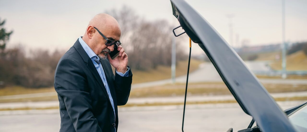 a man using a cell phone while looking under the hood of a car