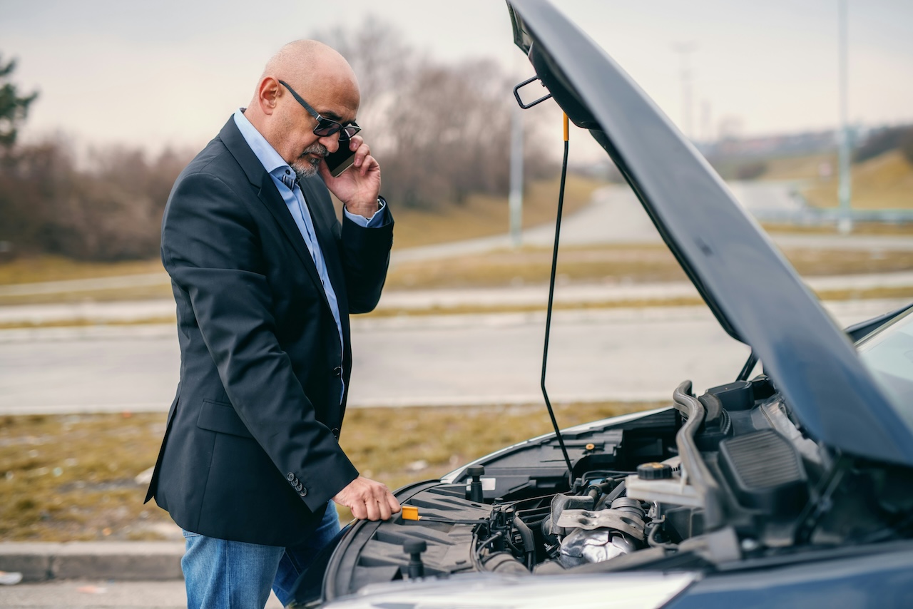 a man using a cell phone while looking under the hood of a car