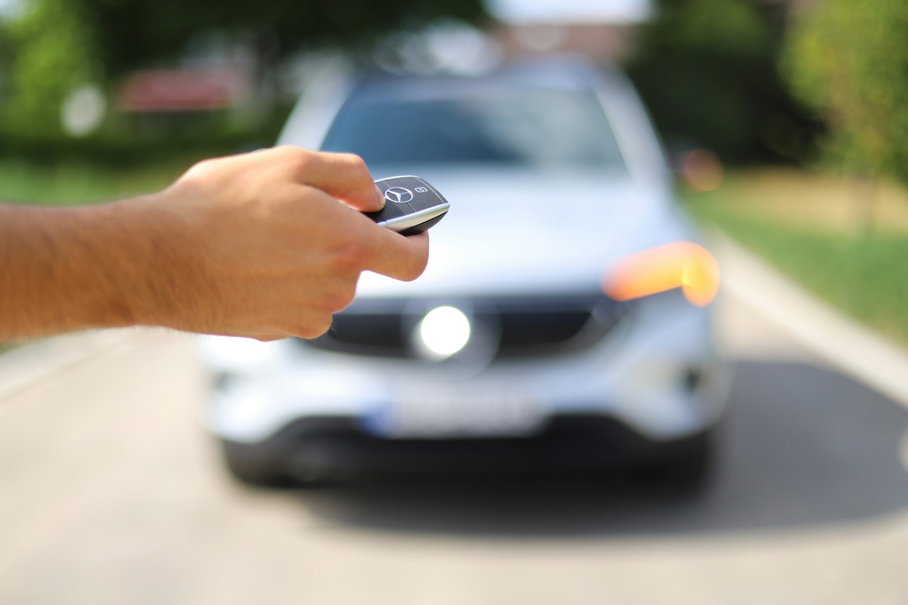 Closeup of a person's hand holding car keys. A car is visible in the background.