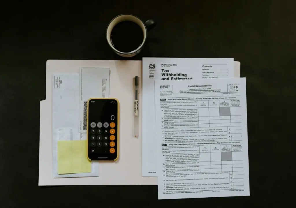 Bird view of a table with smartphone, coffee, pencil and documents on it. The calculator shown on the smartphone and it looks like person is doing his taxes.