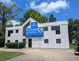 Exterior view of a white two-story office building with a blue law firm sign reading “Huffman & Huffman, P.A.” displayed on the front facade under a clear blue sky.