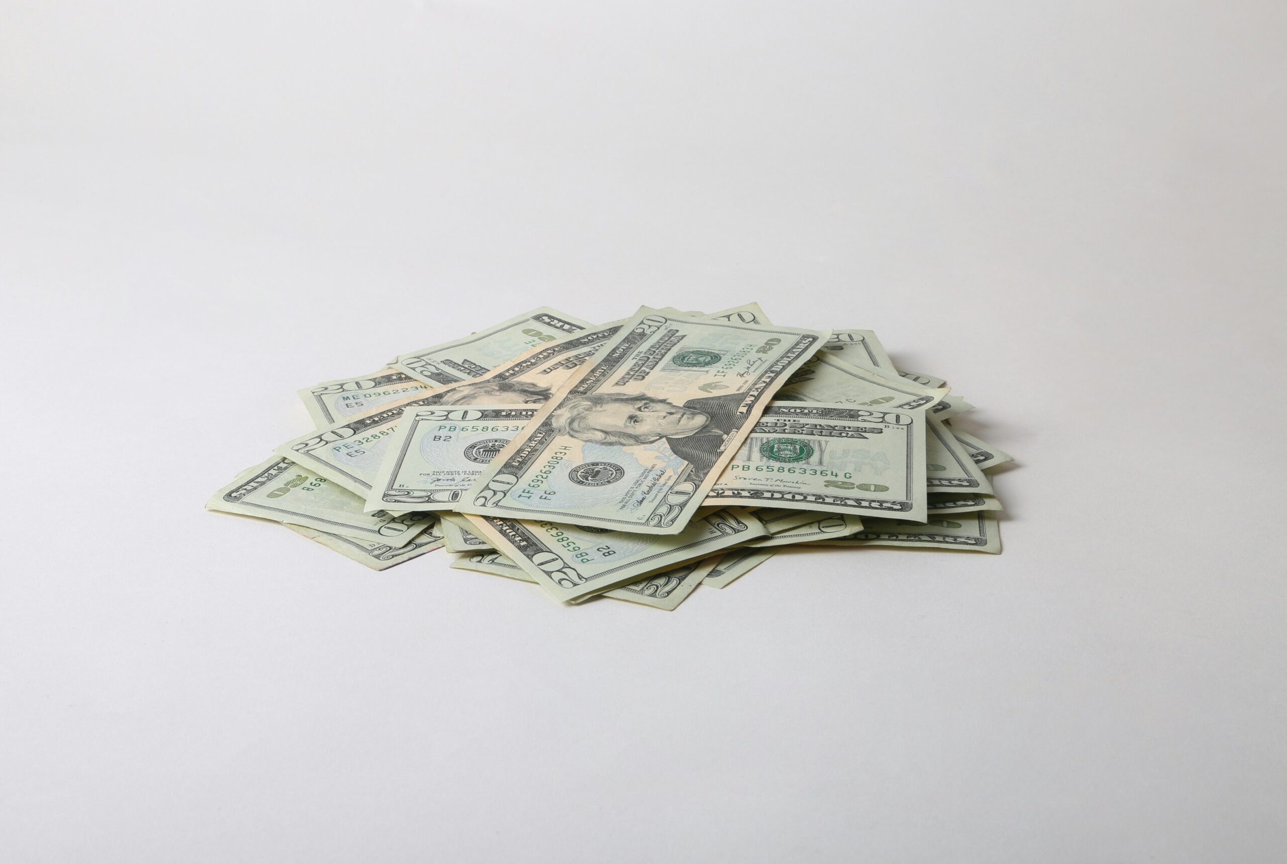 A scattered pile of U.S. twenty-dollar bills laid out on a plain light surface, with the notes overlapping in a loose stack.