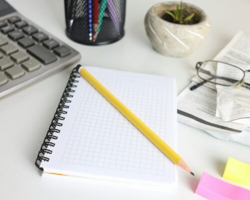 A notepad, pencil, and calculator arranged neatly on a wooden desk, ready for calculations and note-taking.