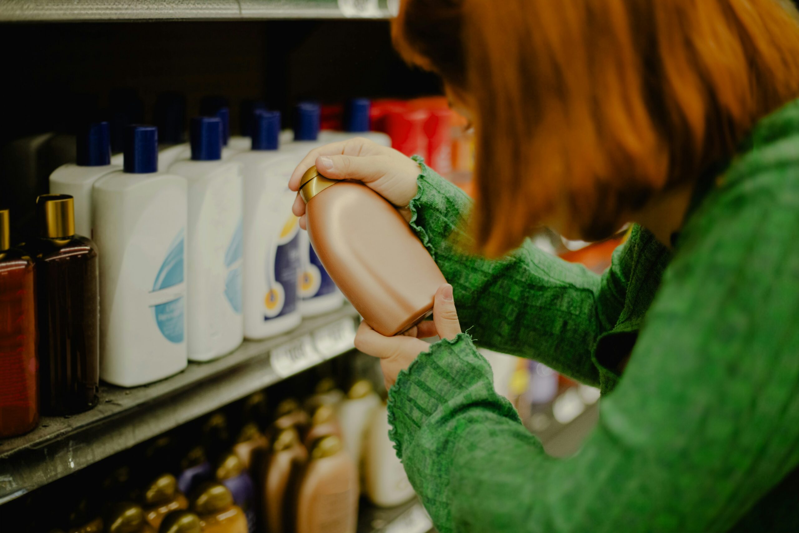 A woman examines a bottle of shampoo while standing in a brightly lit bathroom.