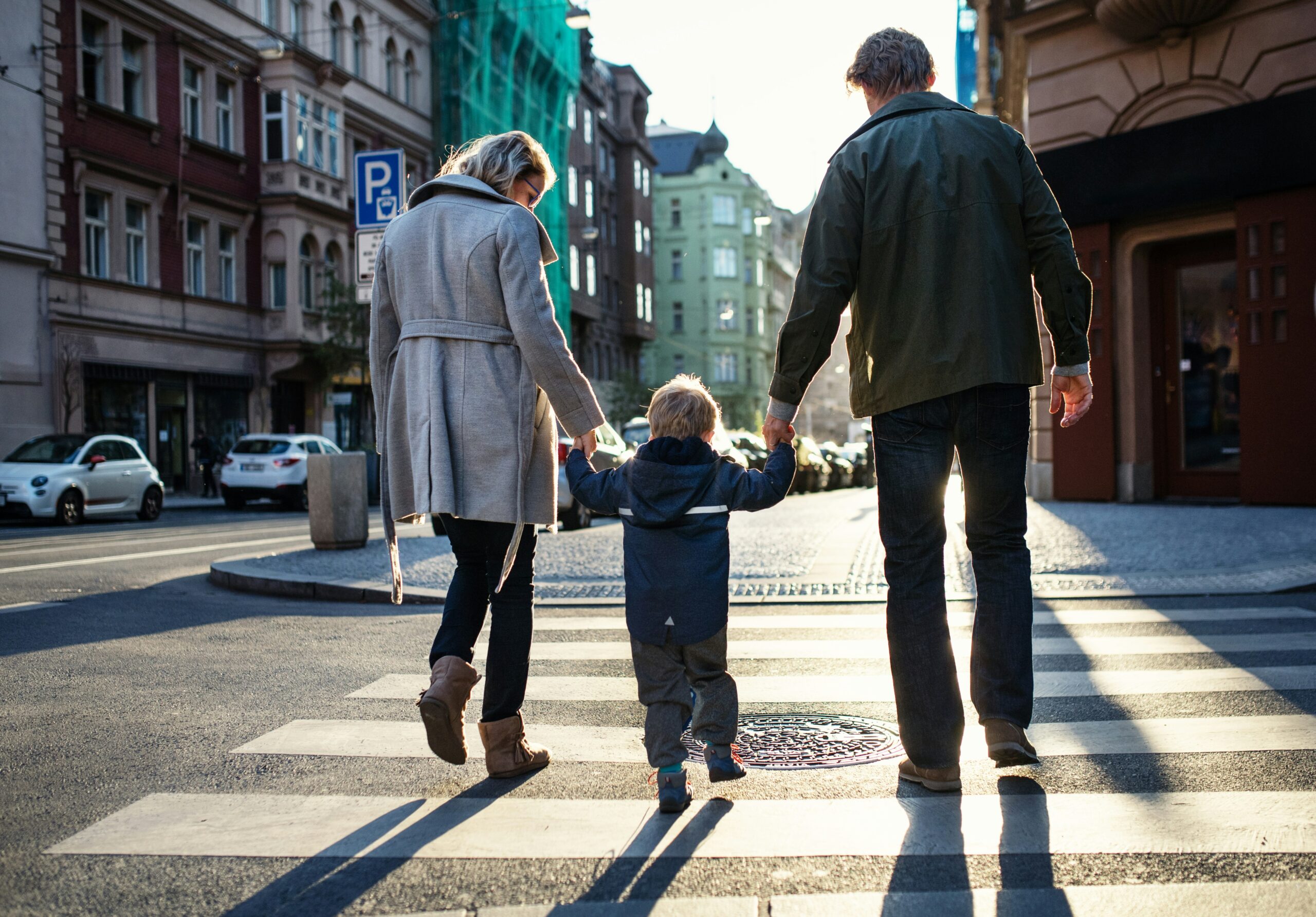 A man and woman hold hands with a child as they cross a street together.