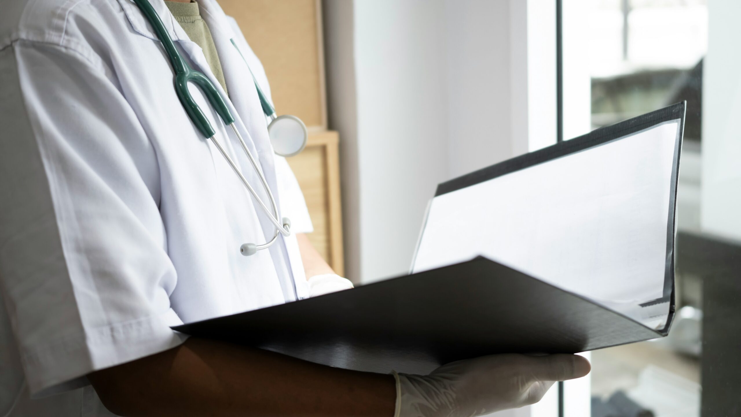 A doctor holding a clipboard attentively examines a patient during a consultation in a medical office.