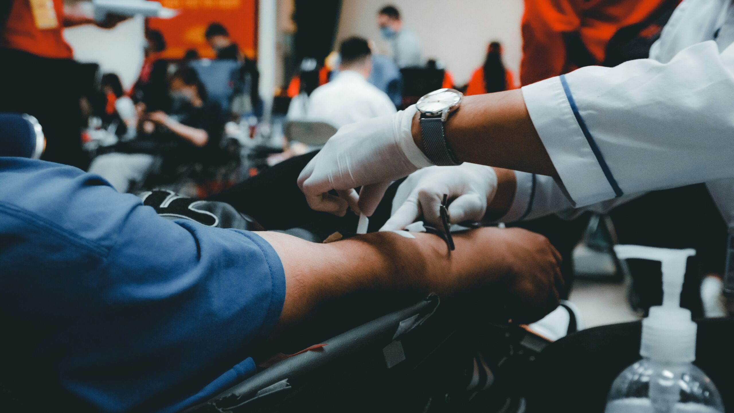 A person sitting in a chair while a healthcare professional draws blood from their arm.